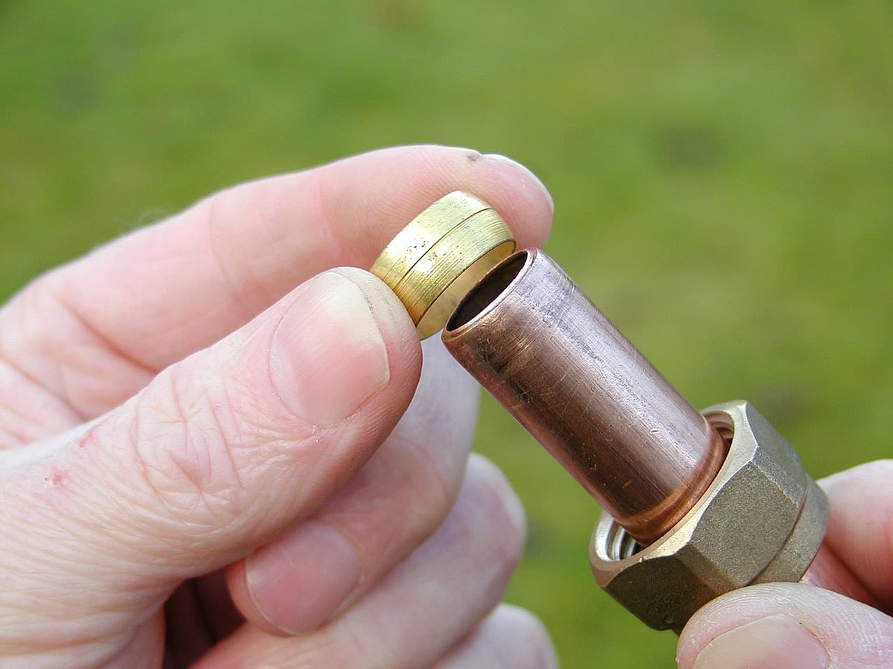 Fingers holding a brass olive and nut on a length of copper pipe