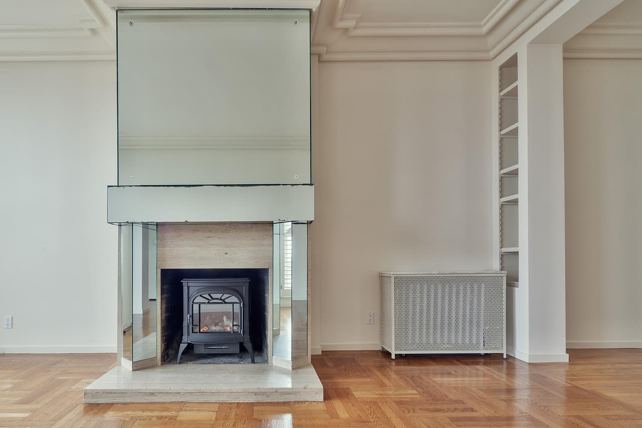 A fireplace with a stove insert in a bright white room with a radiator cover