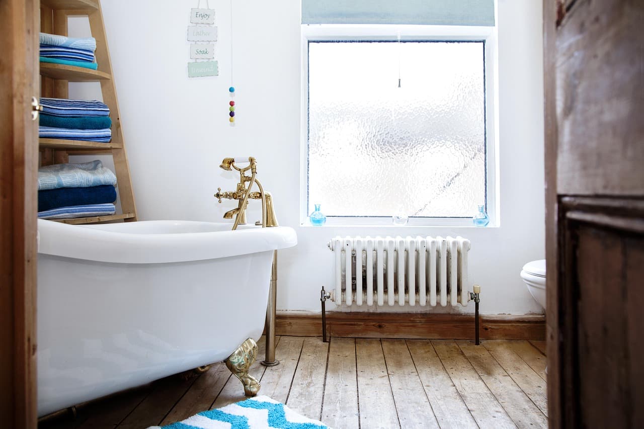 A bathroom with a column radiator under the window beside a roll-top bath