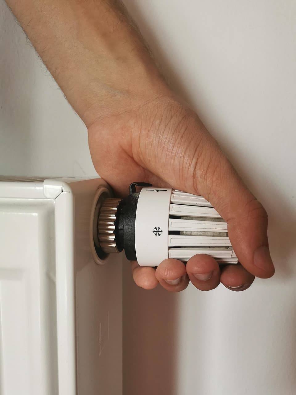 A hand turning a thermostatic valve on a white radiator