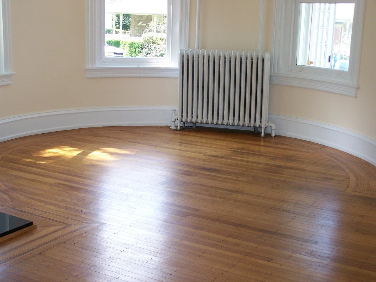 An empty bay-windowed room with a column radiator and a wooden floor